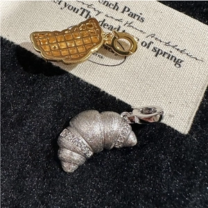 Detail of silver croissant pendant and golden waffle charm on a textured background
