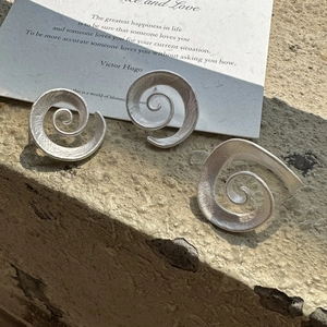 Three minimalist matte silver spiral earrings on stone base with artistic card background