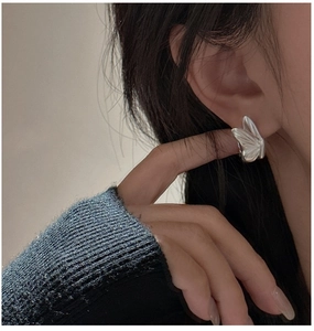 Close-up of matte silver butterfly earring worn on ear with fine wing textures