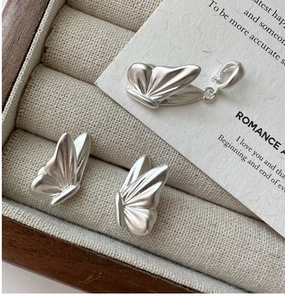 Detailed close-up of matte silver butterfly jewelry set with fine wing textures on fabric