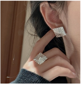 Close-up of square silver rings and earrings with radial pleated metal texture on model