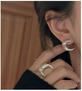 Detailed shot of knotted silver moon ring and stud earring on hand with black outfit
