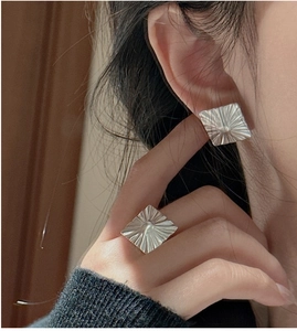 Detailed view of matte silver square earrings with a radiant sunburst texture