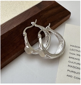 Macro detail of ripple texture silver hoop earring featuring a translucent white gemstone