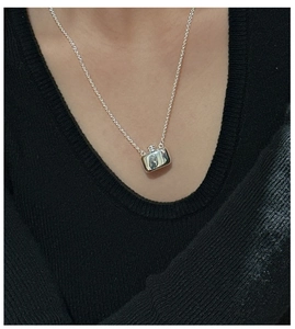 Detail of S925 sterling silver flask pendant necklace worn on a black V-neck sweater