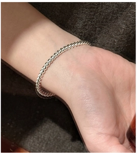 Detailaufnahme eines minimalistischen, gedrehten silbernen Armreifs am Handgelenk