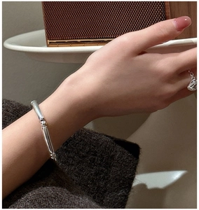 Close-up of a minimalist silver bamboo-style bracelet on a woman's wrist with vintage background