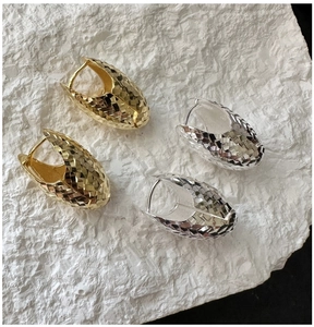 Detail of diamond-cut textured gold and silver hoop earrings on a white stone background