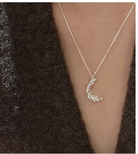 Détail de la texture lave sur pendentif lune argenté porté sur un pull sombre