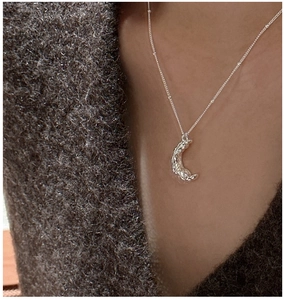 Vue détaillée du collier pendentif lune texturé porté sur un pull en maille gris foncé