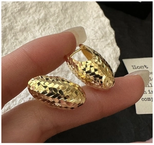 Detail of diamond-cut texture on gold oval hoop earrings held for scale