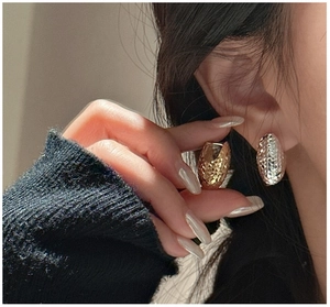 Macro detail of silver and gold oval hoop earrings with textured diamond-cut finish