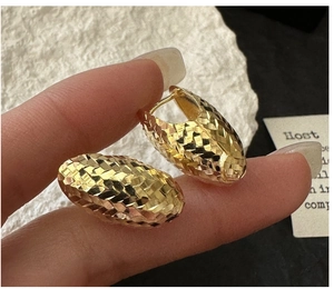 Detail of gold ear hoop with diamond-cut texture and shimmering grid pattern finish