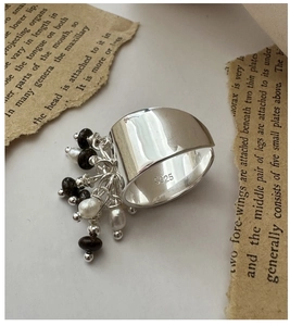 Dettaglio ravvicinato dell'anello in argento S925 con perline e sfondo di libro retrò