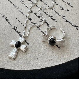 Macro detail of brushed silver butterfly ring and cross necklace with black onyx stones