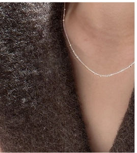 Close-up of minimalist S925 sterling silver beaded necklace on a model wearing brown sweater