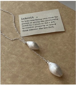 Detail shot of silver water-drop necklace with matte brushed texture on kraft paper