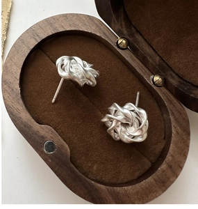 Macro shot of silver matte knot stud earrings with brushed texture in a wooden gift box