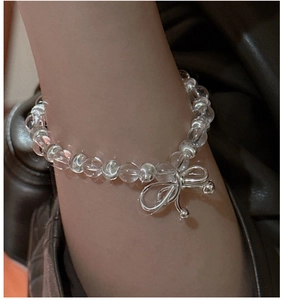Détail du pendentif nœud argenté sur bracelet en perles de cristal blanc au poignet
