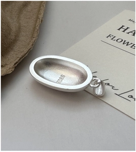 Macro shot of S925 sterling silver oval pendant showing matte texture and purity hallmark
