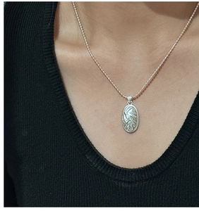 Detail of silver textured oval pendant necklace on beaded ball chain over black knitwear