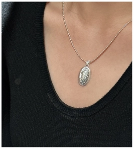 Close-up of S925 sterling silver textured oval pendant on a black knit sweater