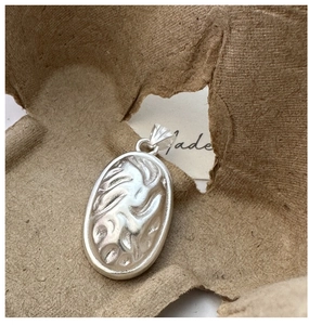 Macro shot of oval silver pendant with abstract fluid texture on textured paper