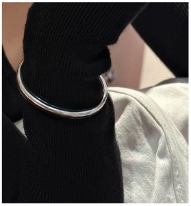 Close-up of a minimalist polished silver bangle worn over black ribbed knit sleeve