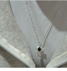 Detail der S925 Silber-Kreuzhalskette mit schwarzem Edelstein auf grauem Strickhintergrund