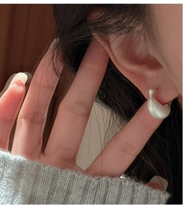 Close-up of minimalist matte silver-tone cocoon earrings worn on ear lobe