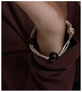 Detail of double-strand silver bracelet with black agate beads on a burgundy sleeve