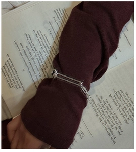 Silver knot OT buckle bracelet worn over a burgundy sleeve on an vintage book background
