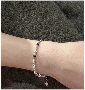 Détail d'un bracelet en perles d'argent avec onyx noirs et breloque cœur au poignet