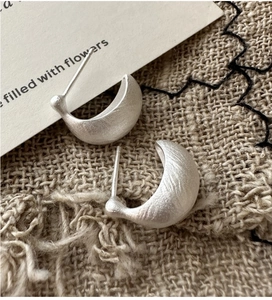 Macro shot of matte silver-plated C-shape earrings with brushed metal texture