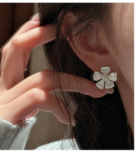 Close-up of matte silver flower stud earrings worn by a model in soft natural lighting
