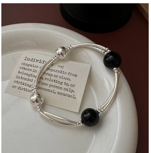 Detail of silver double-layered curved tube bracelet with black onyx beads on ceramic tray