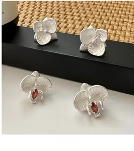Close-up of matte S925 silver orchid earrings with a red ruby centerpiece and floral design