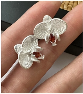 Macro shot of matte silver orchid earrings with orange marquise gemstone detail