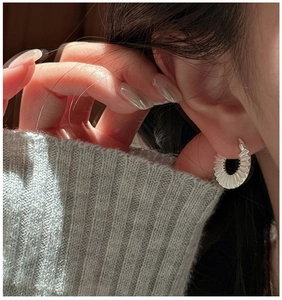 Macro shot of silver plated pleated hoop earrings on model with soft lighting