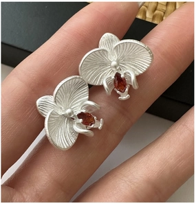 Detail view of matte S925 silver orchid earrings with red marquise gemstone center
