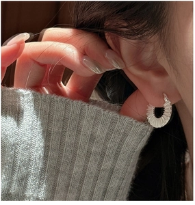 Detail of S925 silver hoop earrings with pleated texture worn on model ear