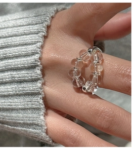 Macro detail of transparent white crystal beaded elastic ring with silver spacers on finger