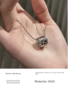 Gros plan d'un pendentif cylindrique martelé en argent S925 tenu à la main sur chaîne