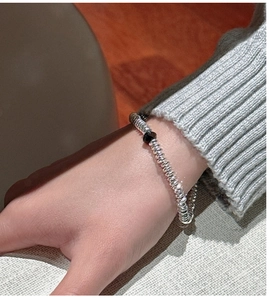 Close-up of S925 silver beaded bracelet with black accent bead on a knit sleeve wrist