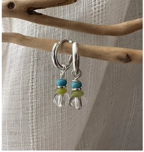 Macro view of S925 silver hoop earrings with blue, green, and clear beads on a wood branch