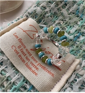 Detailed shot of elastic beaded ring featuring turquoise and green beads on linen pouch