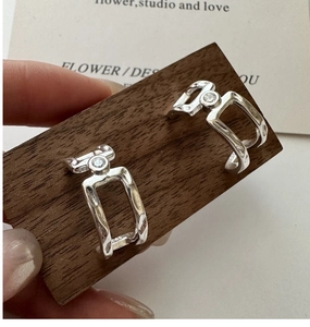 Macro view of S925 sterling silver earrings with perfume bottle silhouette on dark wood