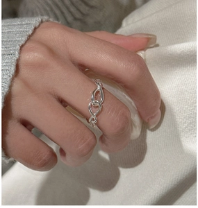 Close-up of S925 sterling silver knotted soft chain ring worn on finger over beige knit background