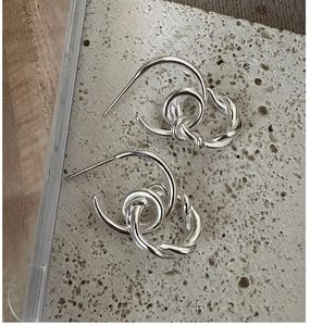 Macro view of silver knotted hoop earrings featuring a minimalist twisted rope design on stone