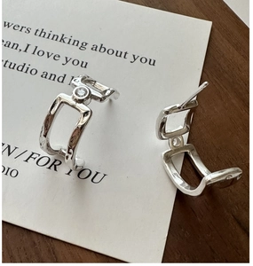 Detail of silver geometric double-layered earrings with a small zircon on white display card